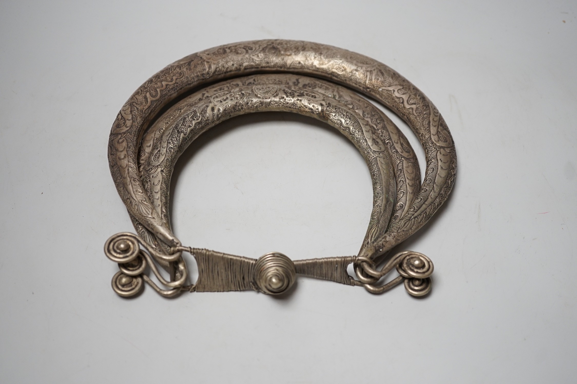 A Chinese Miao white metal triple necklace, repousse worked with dragons and twin fish, 25cm wide
